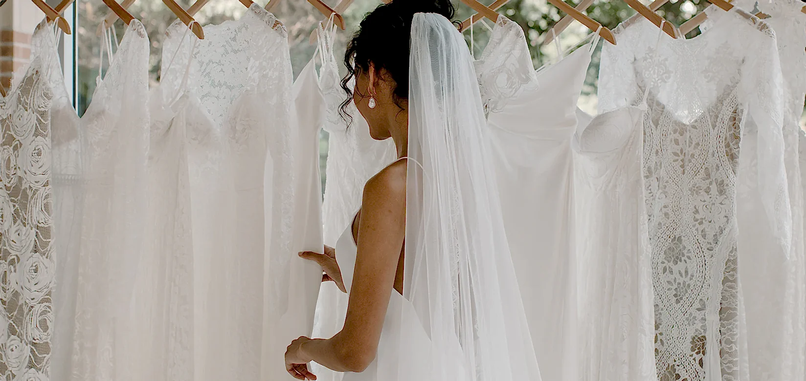 wearing wedding dress looking at rail of wedding dresses
